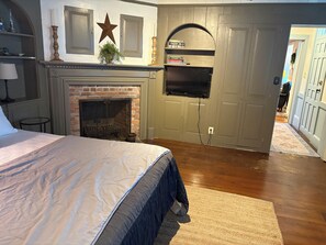 A bedroom with a bed, a fireplace, a television mounted on the wall, and a hallway leading to another room.