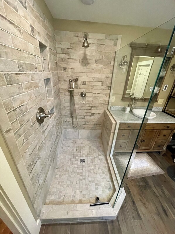 A bathroom with a shower area featuring a brick wall, a glass shower enclosure, and a wooden vanity with a sink.