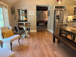 A modern kitchen with stainless steel appliances, a dining area with a wooden table and chairs, and a cozy seating area with a sofa and armchair.