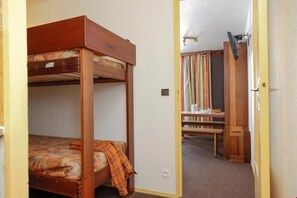 Habitación con literas, cabecero de madera, una mesita pequeña y una estantería.