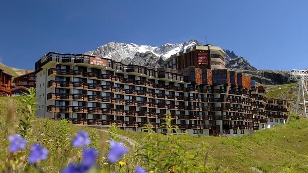 Hotel de vários andares com varandas, com uma paisagem montanhosa ao fundo.
