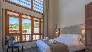 A hotel room with a large window, a bed, a chair, and a view of greenery outside.