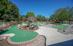 Un campo de minigolf con zonas de juego verdes, un pabellón y una banca.