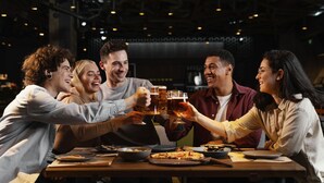 Un grupo de personas brindando con vasos de cerveza en una mesa con comida y una computadora portátil.