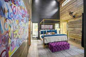 Een kamer met een hemelbed, een paars poef en een muur met kleurrijke graffiti.