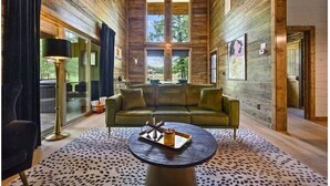 A log cabin interior with a sofa, a round table, and a large window. - Luxury Cabin for Couples + Hot Tub + Fire Pit + Pets (Broken Bow)