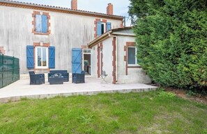 Una casa con patio, muebles de exterior y un árbol grande.
