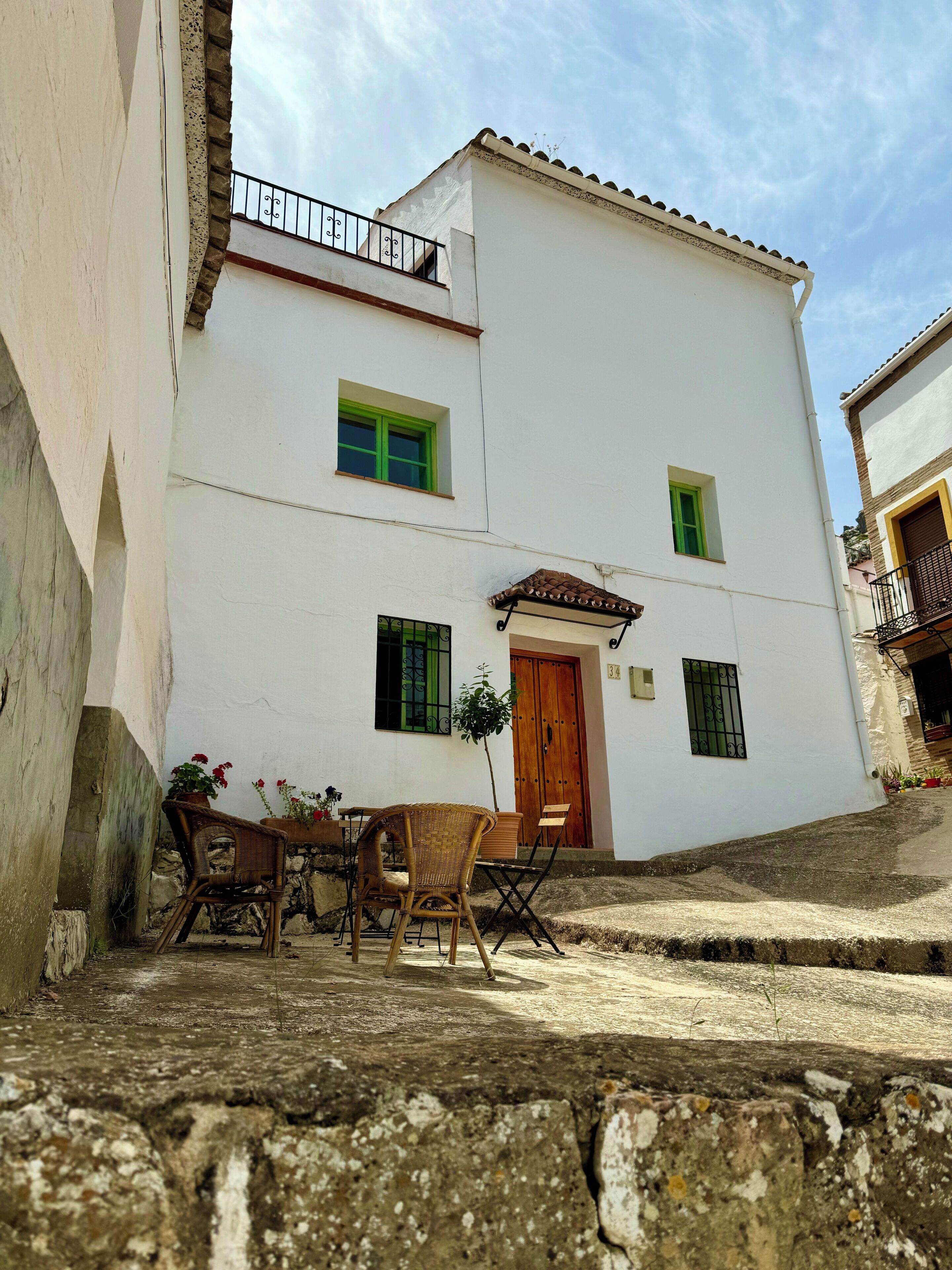 A white building with a wooden door, a balcony with a metal railing, and a small window with green shutters.