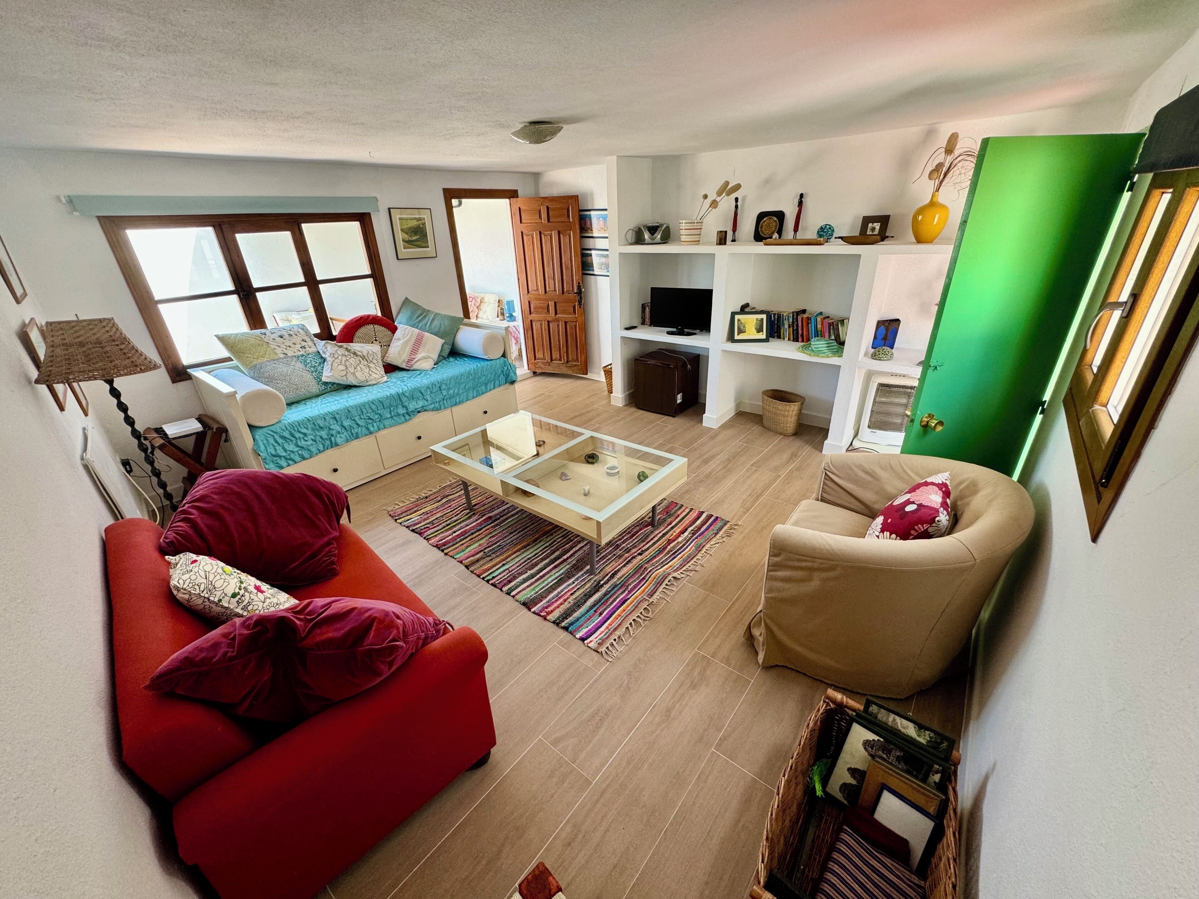 A living room with a sofa, armchair, coffee table, and a TV. There is a bookshelf with books and decorative items.