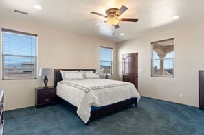 Ein Schlafzimmer mit Bett, Nachttisch, Deckenventilator und Fenstern.