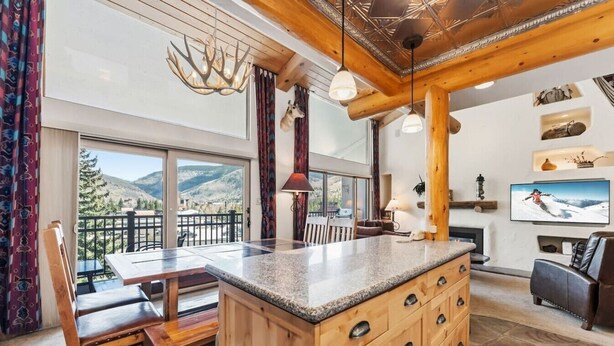 A spacious living area with a large window, a fireplace, and a television. - Lionshead Living | Steps from Gondola + Pool (Vail)