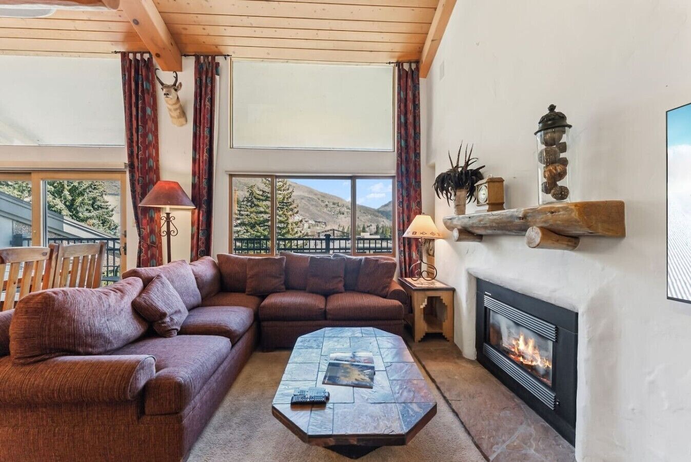 A cozy living room with a fireplace, a sectional sofa, a coffee table, and a view of a mountain landscape.
