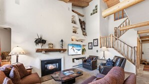 A cozy living room with a fireplace, leather sofas, a coffee table, and a wooden staircase. - Lionshead Living | Steps from Gondola + Pool (Vail)