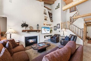 A cozy living room with a fireplace, leather sofas, a coffee table, and a wooden staircase. - Lionshead Living | Steps from Gondola + Pool (Vail)