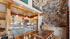 A kitchen with a stone island, wooden cabinets, and a stone wall. - Lionshead Living | Steps from Gondola + Pool (Vail)