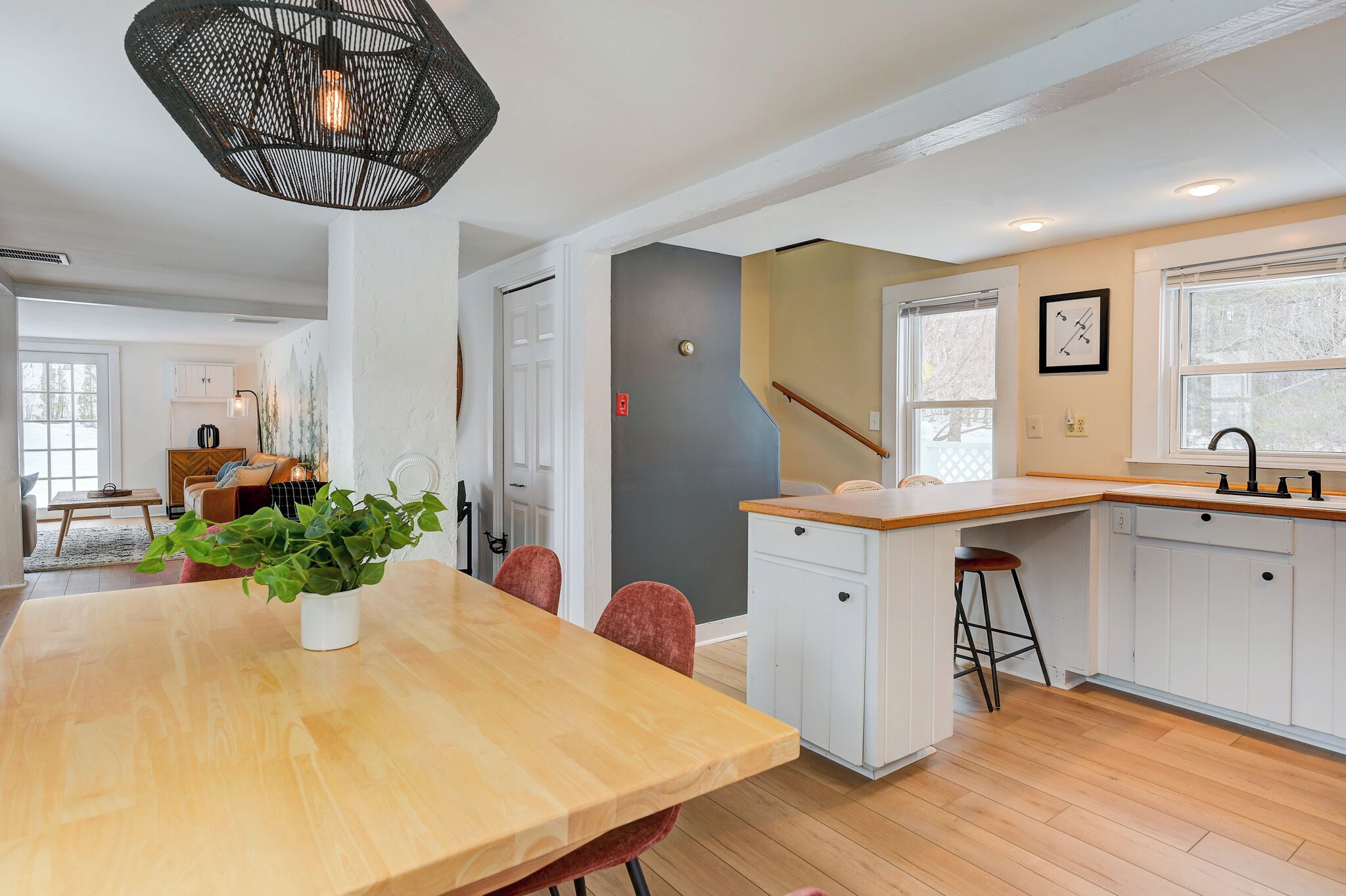 Une cuisine moderne avec des meubles blancs, une table à manger en bois et un luminaire suspendu.