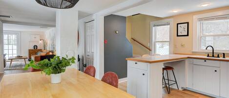 Une cuisine moderne avec des meubles blancs, une table à manger en bois et un luminaire suspendu.
