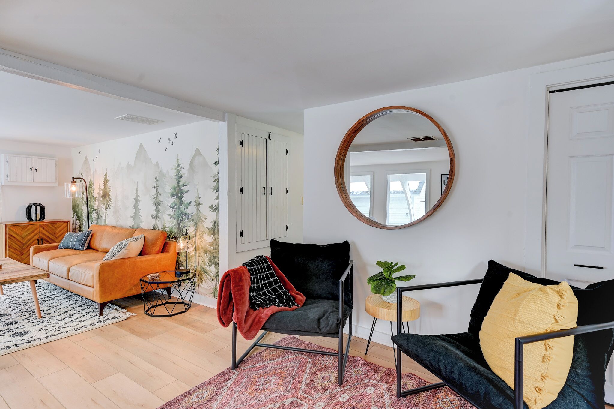 Ein modernes Wohnzimmer mit einer Couch, einem Sessel, einem runden Spiegel und Bergblick durch ein Fenster.