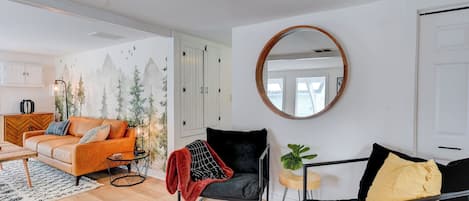 Ein modernes Wohnzimmer mit einer Couch, einem Sessel, einem runden Spiegel und Bergblick durch ein Fenster.