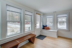 Ein Zimmer mit großen Fenstern, einer Bank, einem Heizkörper und einer Tür.