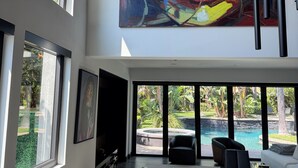 A modern interior with large windows, a pool view, and a prominent abstract painting.