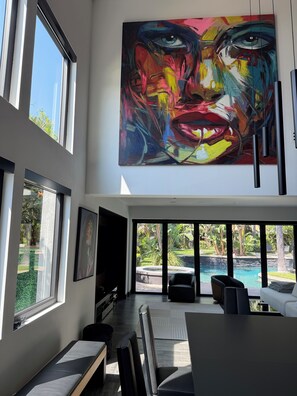 A modern interior with large windows, a pool view, and a prominent abstract painting.