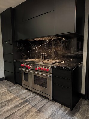 A modern kitchen with black cabinetry, a stainless steel stove, and a marble countertop.