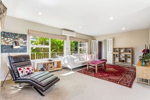 Ein geräumiges Wohnzimmer mit Ledersessel, weißem Sofa und einem roten Teppich mit Muster.