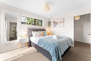 A bedroom with a bed, bedside lamps, a window, a door, and a wall-mounted artwork. - Charming single-level home - just moments from the beach,  sun-soaked garden. (Auckland)