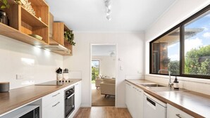 A modern kitchen with white cabinetry, wooden countertops, and a large window. - Charming single-level home - just moments from the beach,  sun-soaked garden. (Auckland)