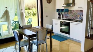 A modern kitchen with a gas stove, oven, and stainless steel range hood. There is a dining area with a table and chairs, and a large window with curtains. - Beautiful cottage with garden Resort Adamo& Eva (Numana)