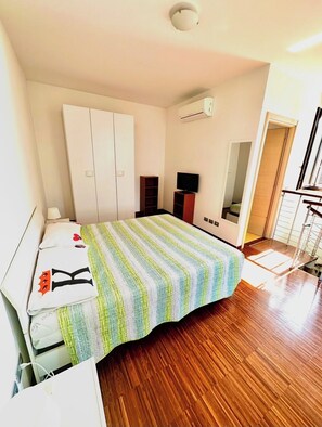 Ein Schlafzimmer mit Bett, Schreibtisch, Kleiderschrank, Fernseher und Klimaanlage.