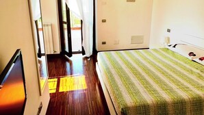 A hotel room with a bed, a television, a window with curtains, and a door leading to a balcony. - Beautiful cottage with garden Resort Adamo& Eva (Numana)