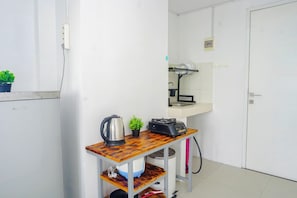A compact kitchen with a refrigerator, a small table with a kettle and a plant, a sink, and a door. - Cozy And Simple 1Br At Apartment Grand Sentraland Karawang (Karawang)