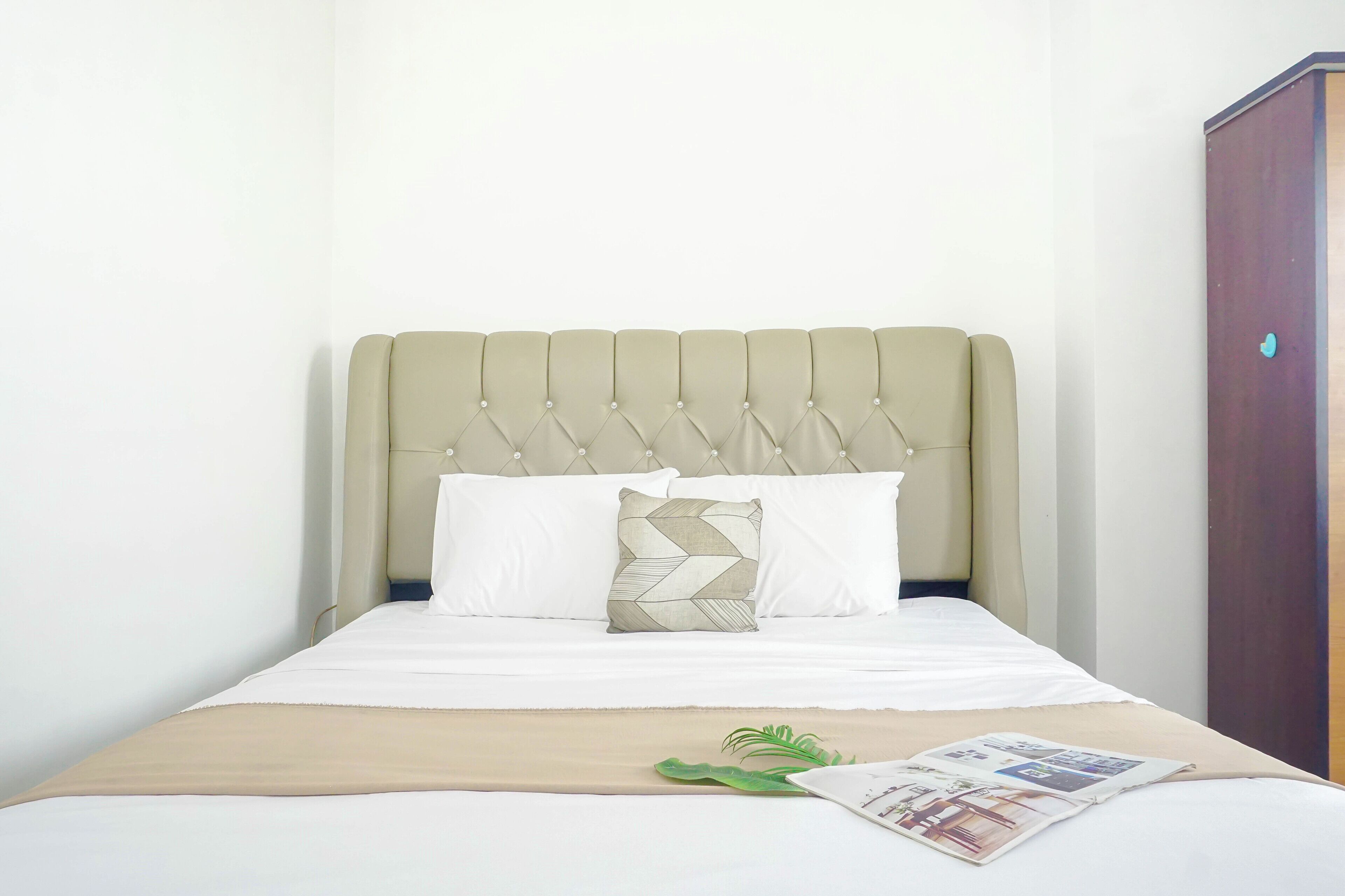 Una cama con cabecera capitonada, ropa de cama blanca y almohada estampada.