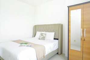 Ein ordentlich bezogenes Bett mit einem beige farbenen Kopfteil, weißer Bettwäsche und einer Zeitschrift darauf.