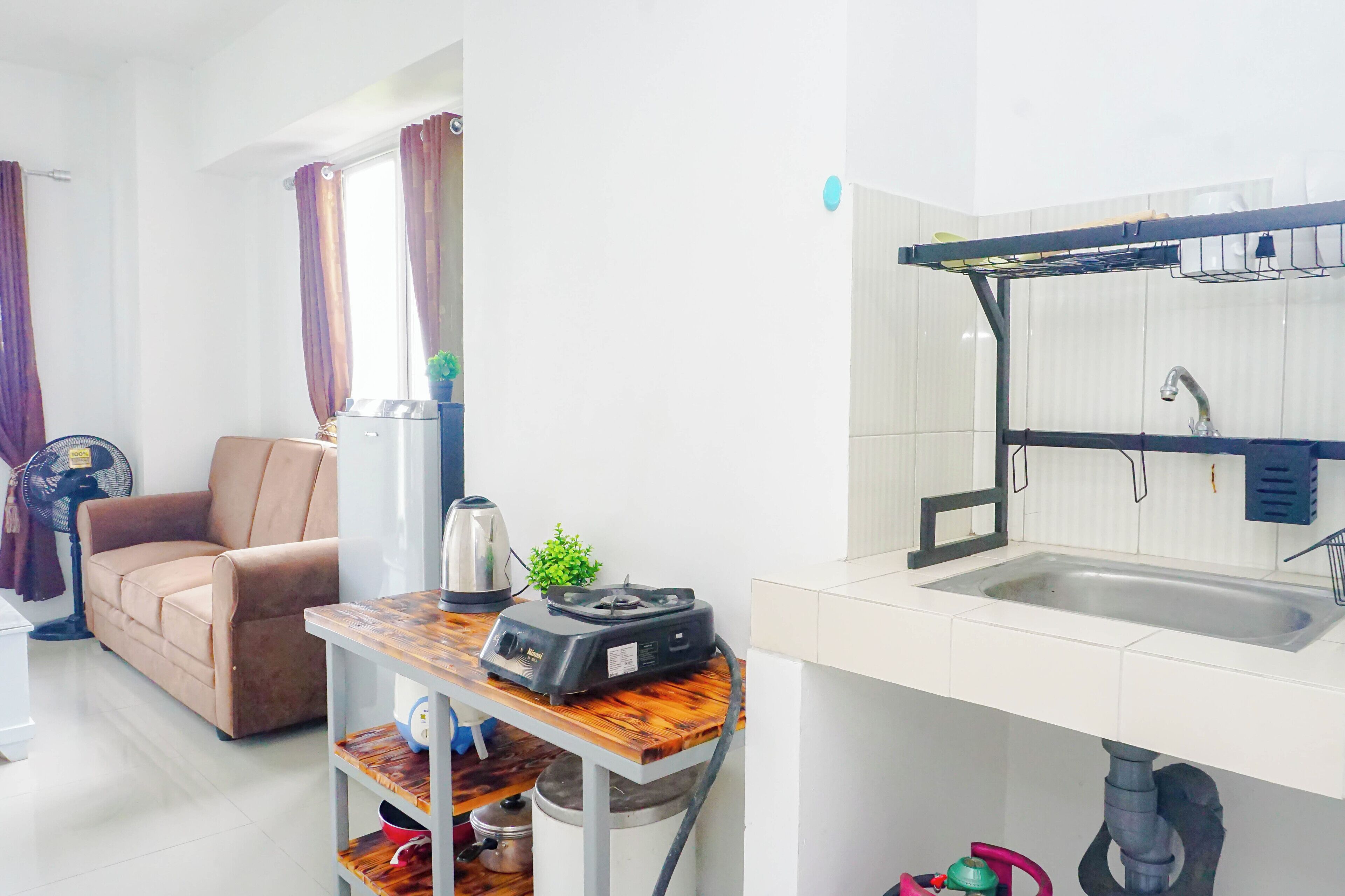 En kompakt opholdsstue med tekøkken, sofa, ventilator og et lille bord med elkedel.