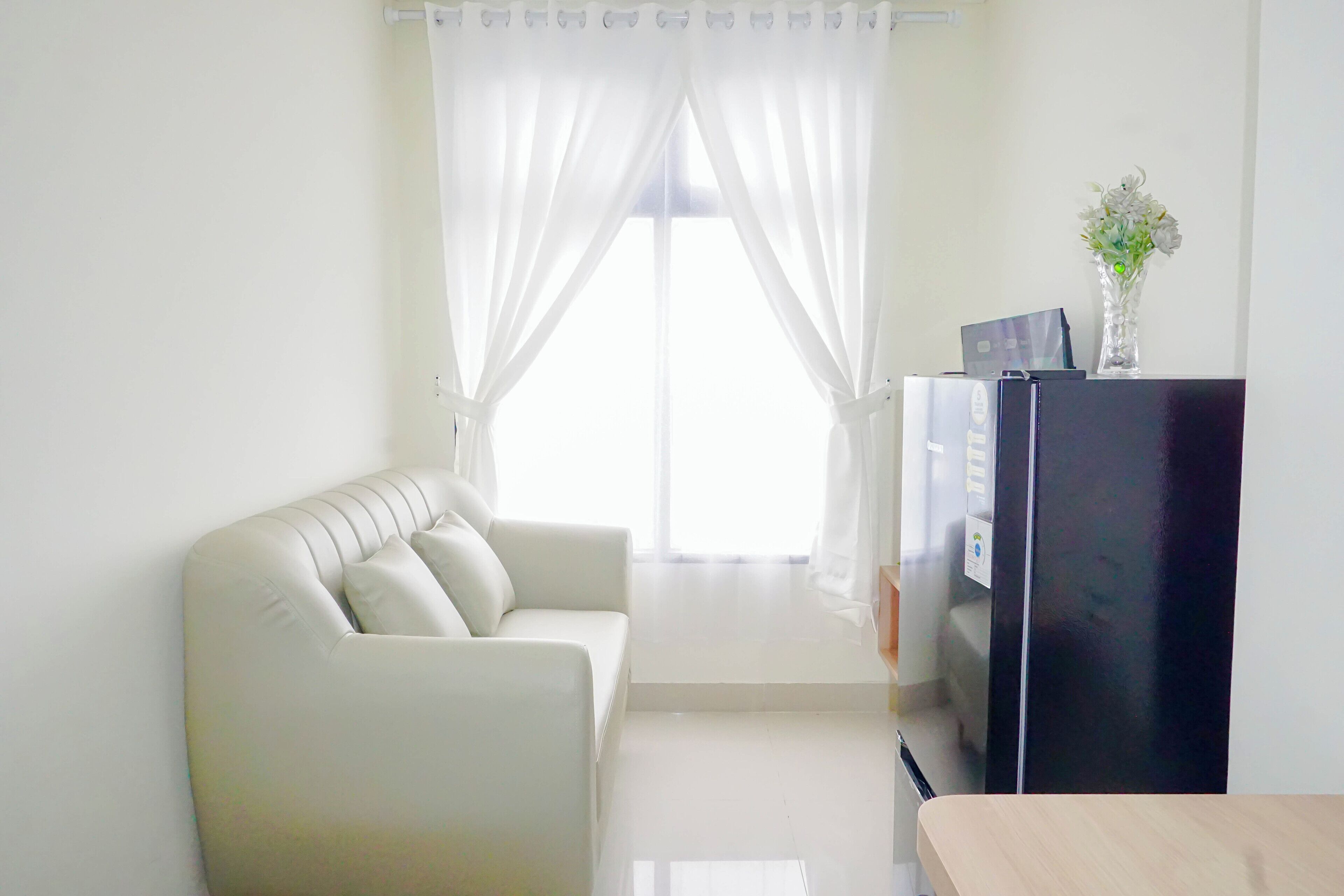 A living room with a sofa, a black refrigerator, and a vase with flowers on a table.