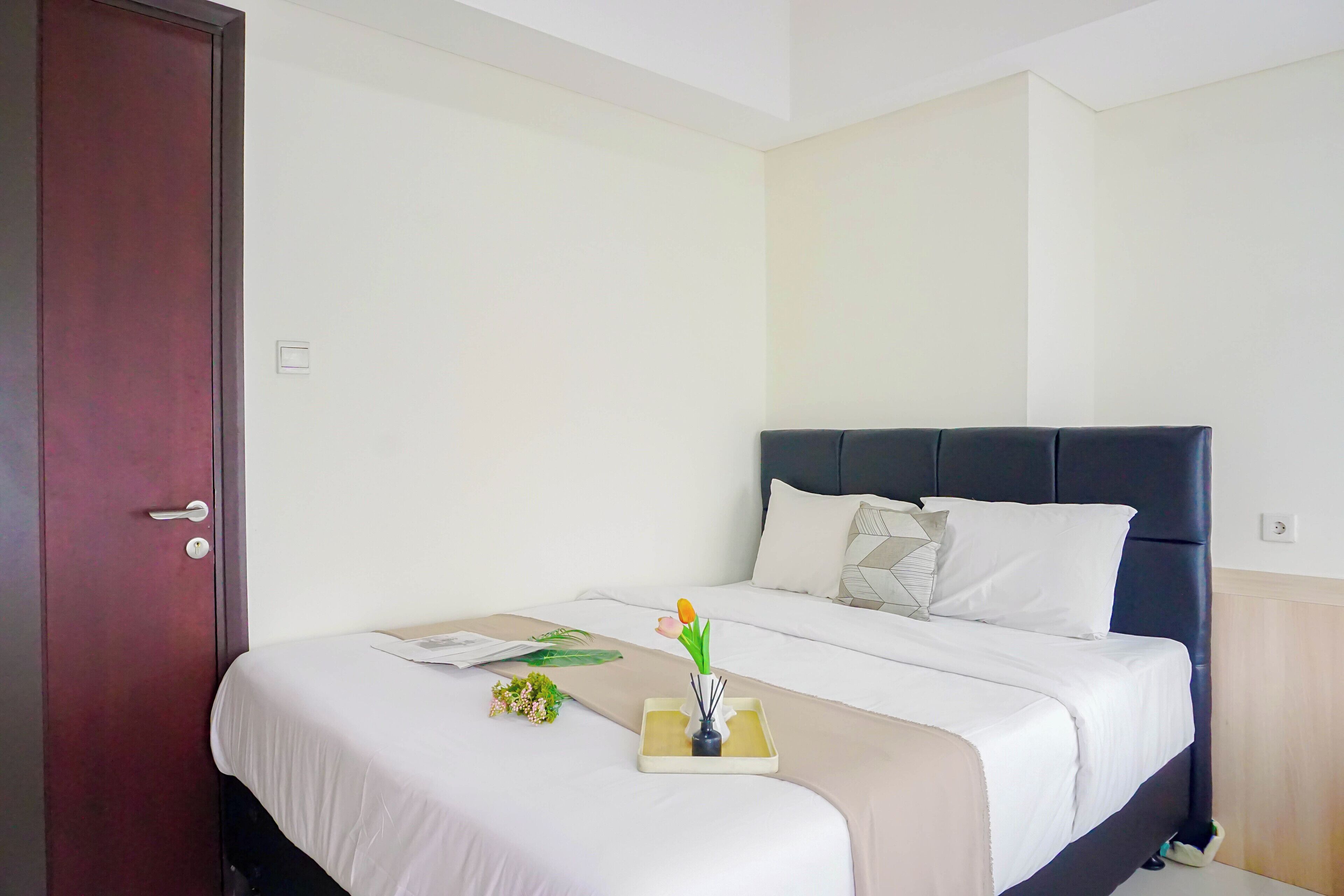 A neatly made bed with white linens, a dark headboard, and a bedside table with a vase of flowers.