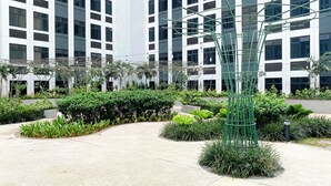 Een modern gebouw met een binnentuin, een metalen sculptuur, weelderige beplanting en een betonnen pad.
