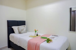 Ein ordentlich bezogenes Bett mit einer weißen Decke, einer rosafarbenen Tagesdecke und einer kleinen Vase mit Blumen.