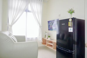 A modern living room with a black refrigerator, white sofa, and a wooden shelf with a potted plant. - Comfy And Bright 2Br At Pollux Chadstone Apartment (Cikarang)