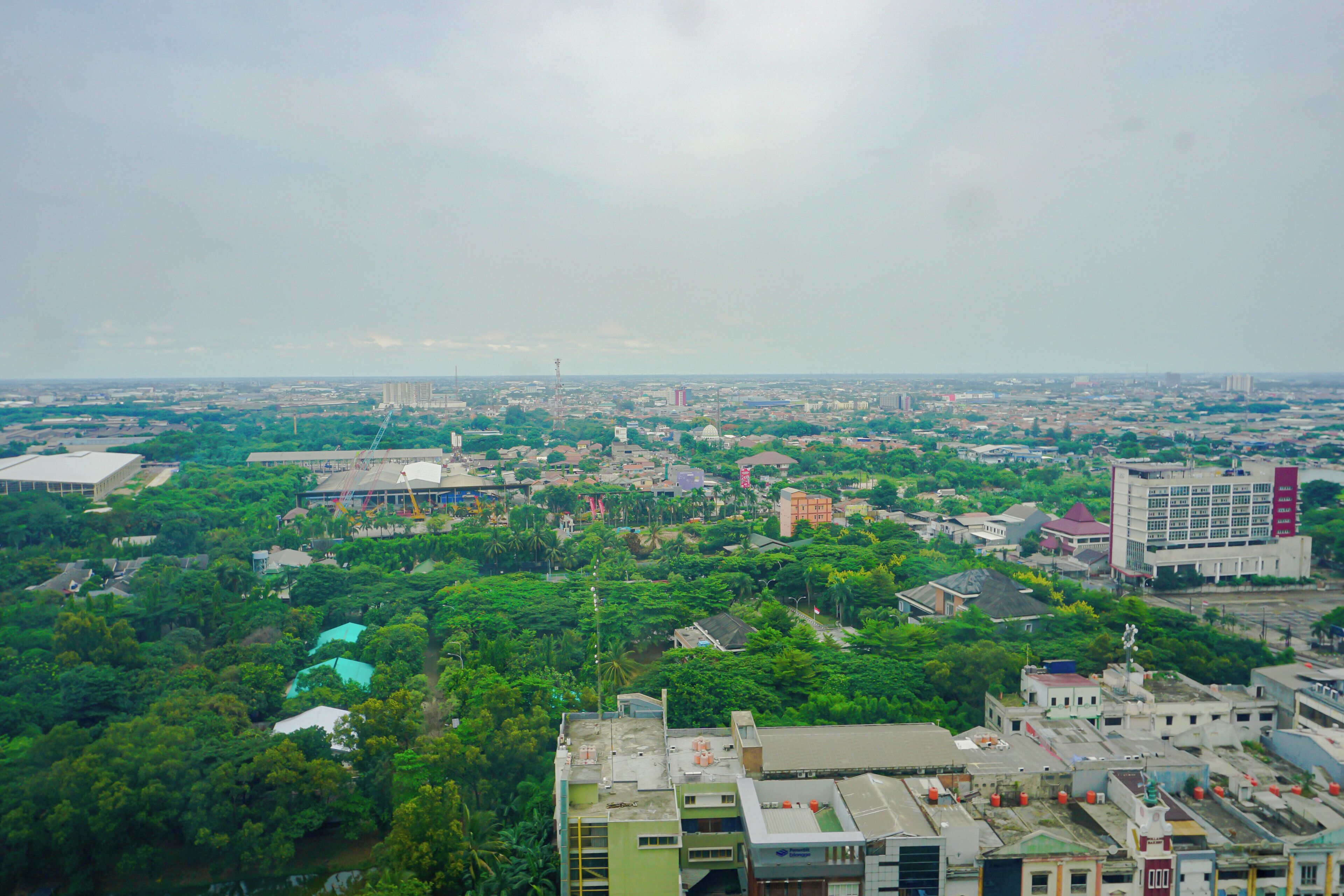 An aerial view of a cityscape with buildings, greenery, and a distant tower.