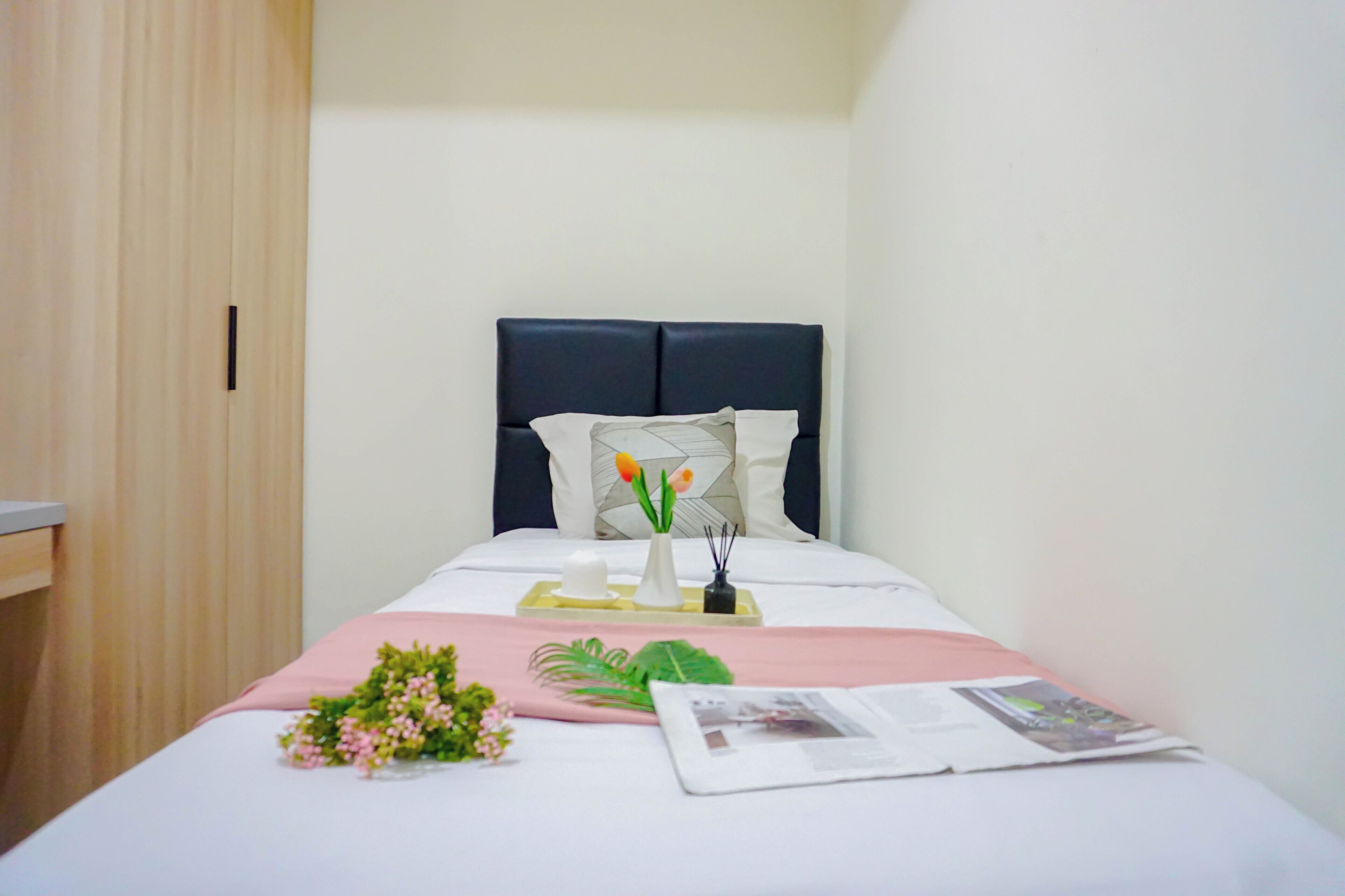 A neatly made bed with a headboard, a bedside table with a lamp, and a small plant.