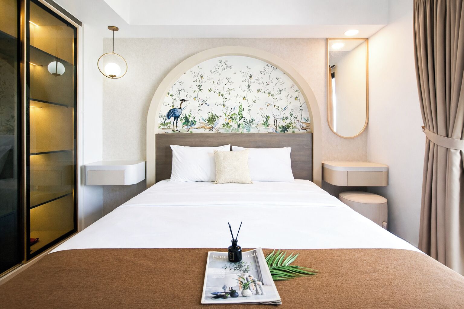 Una camera d'albergo con un letto, un comodino, uno specchio, una TV a parete e una pianta sul davanzale.