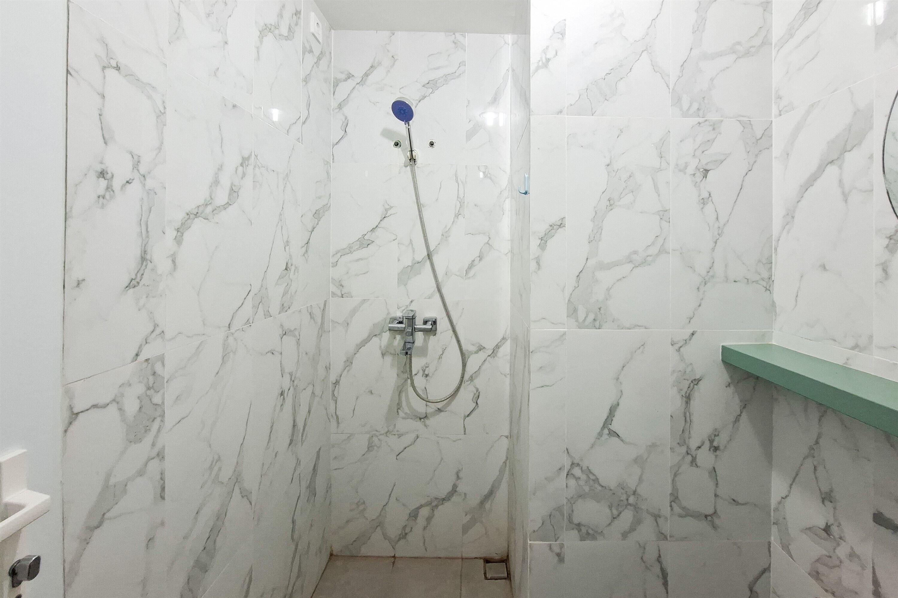 Een badkamer met marmeren wanden, een douche met handdouche en een groen plankje.