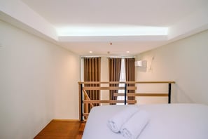 A hotel room with a bed, a wooden headboard, a ceiling light, and a window with curtains. - Best Deal And Homey Studio Loft Apple 1 Condovilla Apartment (Jakarta)