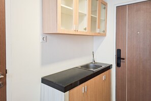 A kitchen with a black countertop, wooden cabinets, a stainless steel sink, and a wooden door. - Airy And Cozy Combined Loft Unit 2Br At Apartment Apple 1 Condovilla (Jakarta)