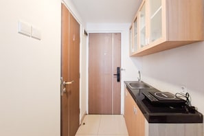 A narrow kitchen with wooden cabinets, a countertop, and a door leading to another room. - Airy And Cozy Combined Loft Unit 2Br At Apartment Apple 1 Condovilla (Jakarta)