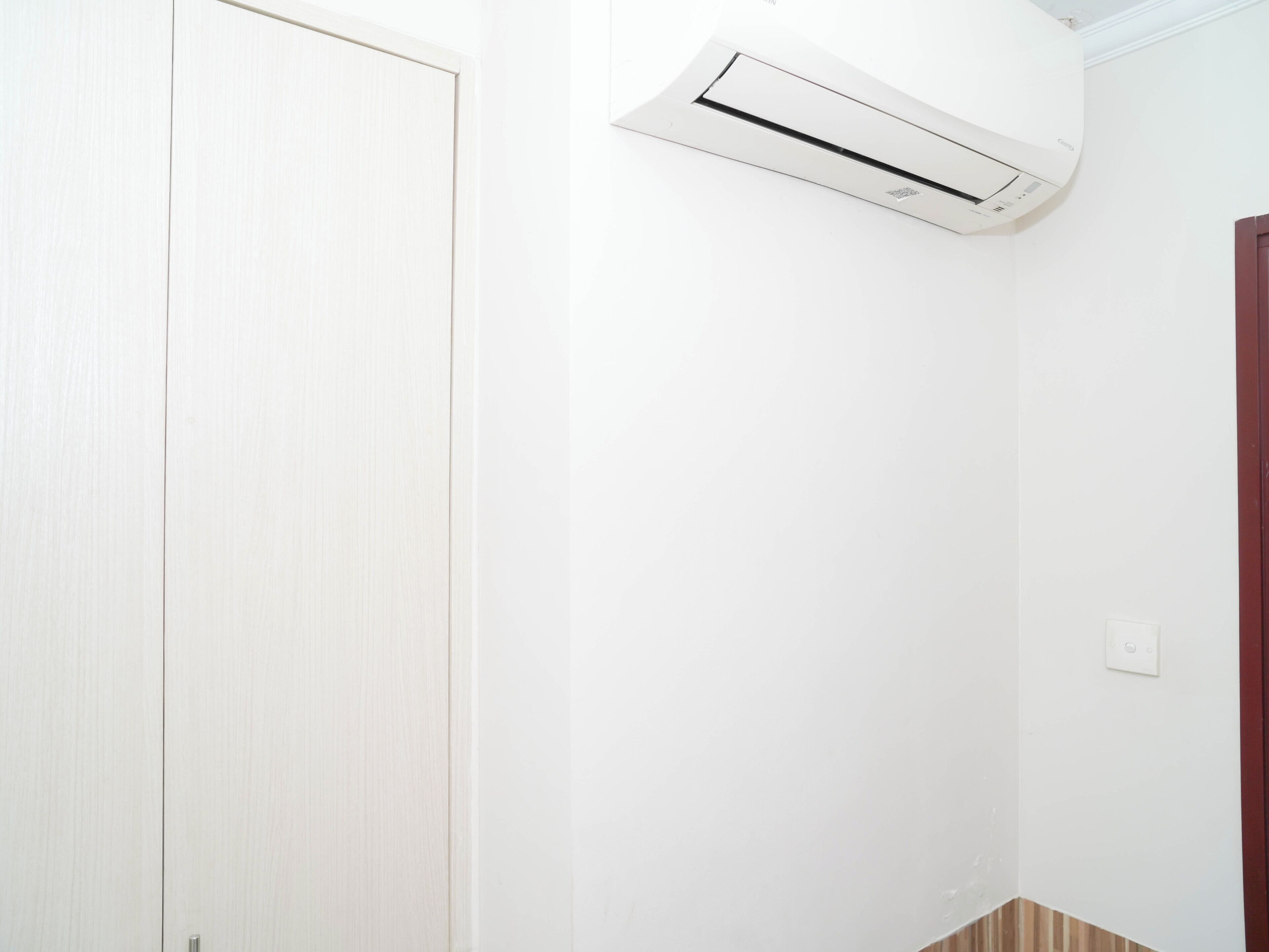Una stanza bianca con una porta chiusa, un condizionatore d'aria bianco fissato al muro e un interruttore sulla parete.